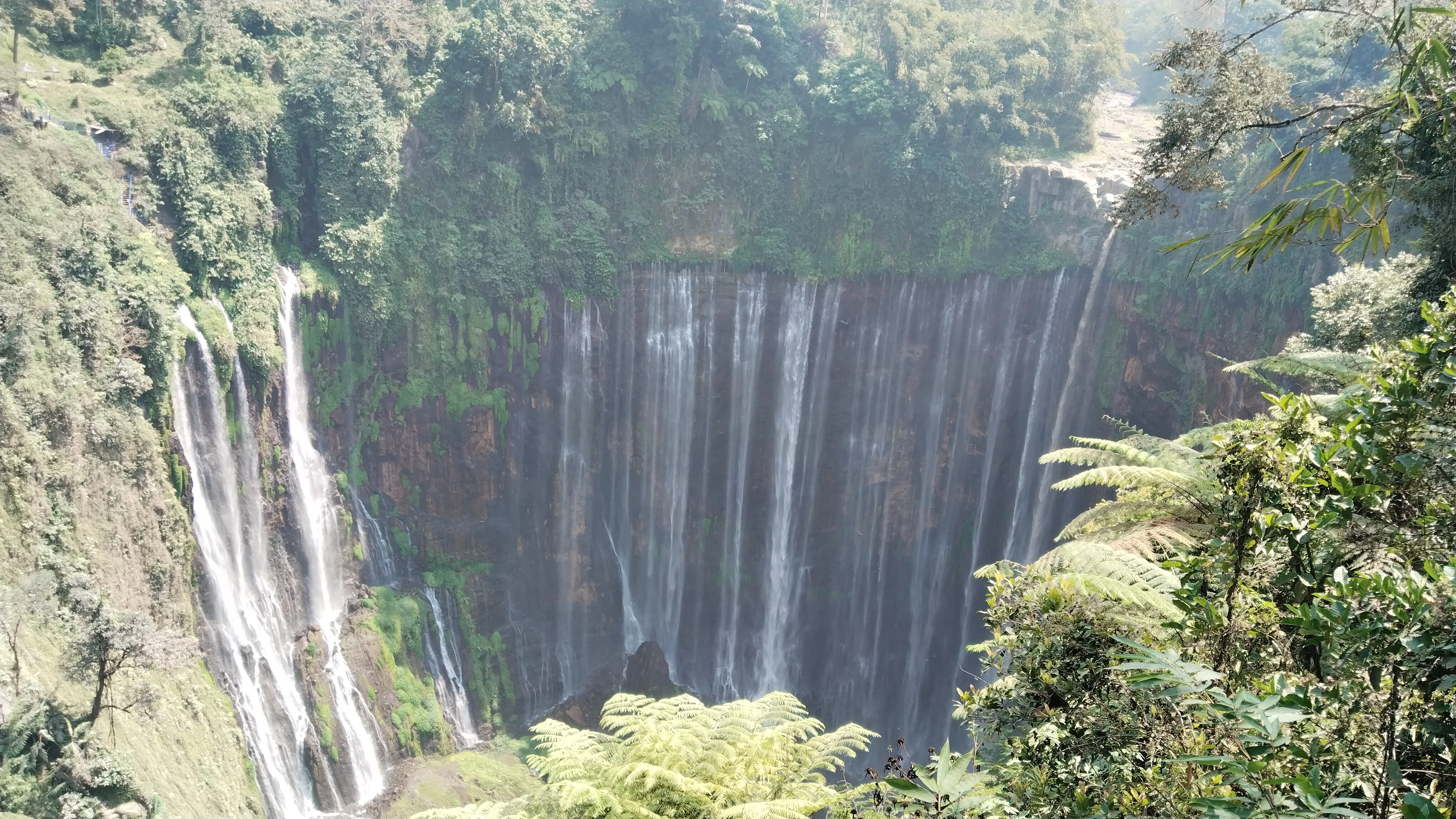 Tumpak Sewu Waterfall cascading down a broad green cliff in East Java, Indonesia.